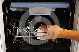 Close-up of a woman`s hand loading dishes, emptying or unloading them from an open automatic built-in dishwasher with dishes insi
