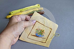 Close up of woman`s hand making cross-stitch on light-brown cotton canvas. Handmade embroidery, set of multi-colored threads. Cop