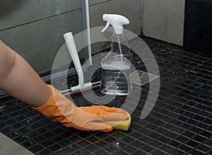 Close up of woman& x27;s hand in orange gloves cleaning dirty shower floor tiles