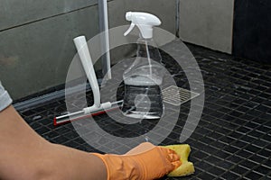 Close up of woman& x27;s hand in orange gloves cleaning dirty shower floor tiles