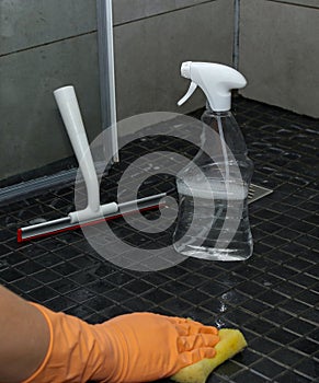 Close up of woman's hand in orange gloves cleaning dirty shower floor tiles