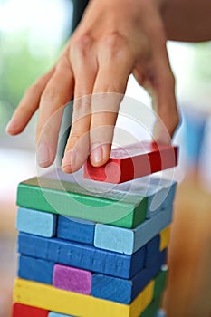 Close-up of woman`s hand pick the red stack on the wooden tower game in morning light , playing and learning background concept