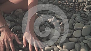 Close up of a woman`s hand picking up a stone, and then throwing it from a palm on the beach.