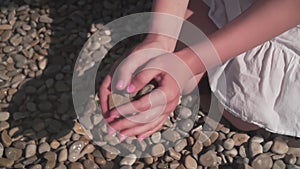 Close-up of a woman`s hand picking up a stone, and then throwing it from a palm on the beach.