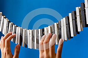Close-up of a woman`s hand playing the imaginary piano made from clothes pins on blue paper background