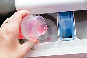 Close-up of a woman& x27;s hand pouring laundry detergent into a washing machine