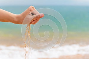 Close-up of a woman& x27;s hand releasing falling sand. Sand flows through the hand against the backdrop of the turquoise