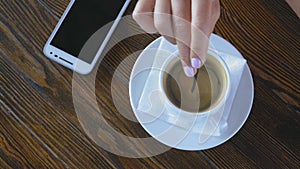 Close-up, woman`s hand with spoon aid stir sugar in a coffee cup on a wooden table