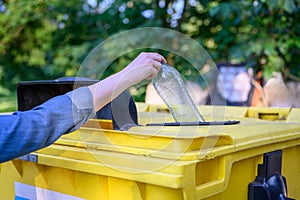 Close-up of a woman`s hand tossing an empty plastic bottle into a trash can