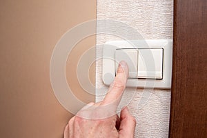 Close-up of a woman`s hand turning the light on or off with a wall switch, front view, close-up, copy space
