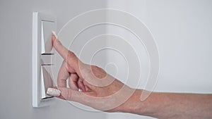 Close-up woman's hand turns off the white wall light switch,copy space,space for text.Concept of energy saving electricity