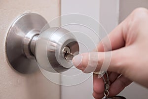 Close up of woman`s hand using key for unlocking or locking the white door