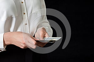 Close-up of woman`s hand in white shirt, holding 100 dollar banknotes, isolated on black background. Business concept