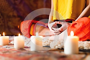 Close-up of woman`s hand in yoga lotus pose meditating in a crafting room with candles