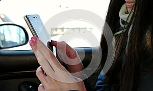 Close-up woman`s hands chatting her cellphone sitting in the car. Side view.