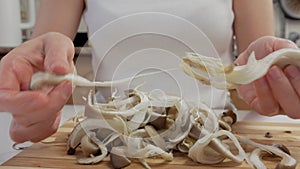 Close-up of a woman's hands dividing fresh mushrooms into fibers and throwing them into dishes