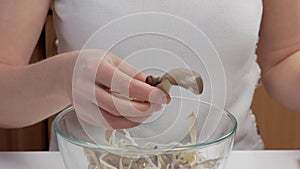 Close-up of a woman's hands dividing fresh mushrooms into fibers and throwing them into dishes