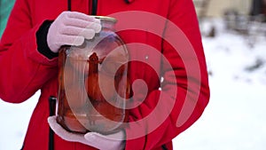 Close up of woman's hands in gloves holding canned tomatoes in garden in wintertime. Unrecognizable female holding