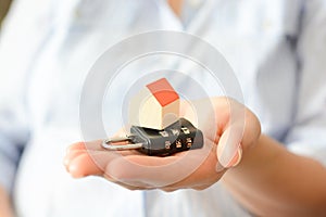 Close-up of woman's hands holding a small model house on top of a cipher lock