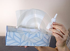 Close up of woman's hands holding a tissue box and a nose spry bottle, white background