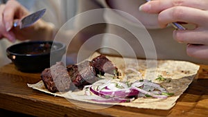 Close up woman's hands with knife and fork cutting meat in dish on table in a restaurant