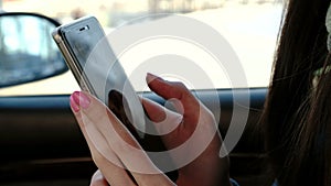 Close-up woman`s hands messaging her cellphone sitting in the car. Side view.