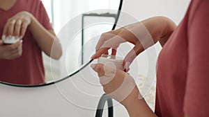 Close-up of woman`s hands opening cream standing in bathroom in front of mirror