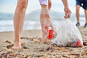 Close-up of a woman& x27;s hands picking up plastic trash into a bag on the beach