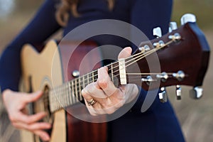Close-up of woman's hands playing an acoustic guitar. Outdoor leisure, creative evening, warm autumn, sunset.