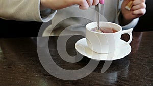 Close-up of the woman`s hands pour sugar into a Cup of tea and stir it with a spoon.