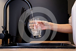 Close-up of a woman's hands pouring a glass of fresh water from the tap in the kitchen. Woman drinking a glass of