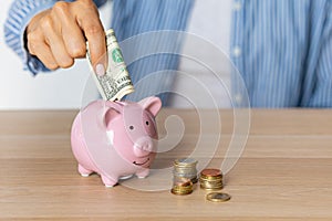 Close-up of a woman\'s hands put dollar paper money in a piggy bank, next to a calculator on the table. economy, crisis and