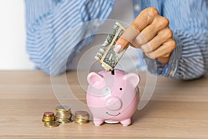 Close-up of a woman\'s hands put dollar paper money in a piggy bank, next to a calculator on the table. economy, crisis and