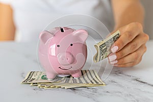 Close-up of a woman's hands put dollar paper money in a piggy bank, next to a calculator on the table. economy, crisis and