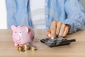Close-up of a woman\'s hands put a euro coin in a piggy bank, next to a calculator on the table.saving money in a crisis and