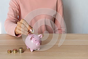 Close-up of a woman's hands putting a euro coin in a piggy bank, saving money in a crisis and inflation