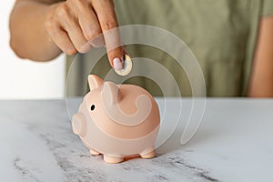 Close-up of a woman's hands putting a euro coin in a piggy bank, saving money in a crisis and inflation