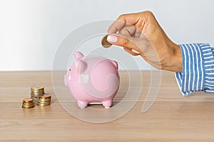 Close-up of a woman's hands putting a euro coin in a piggy bank, saving money in a crisis and inflation