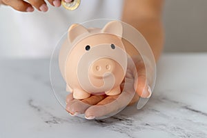 Close-up of a woman\'s hands putting a euro coin in a piggy bank, saving money in a crisis and inflation