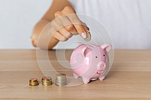 Close-up of a woman's hands putting a euro coin in a piggy bank, saving money in a crisis and inflation