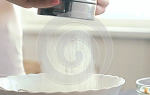 Close-up woman`s hands sift flour through a sieve.