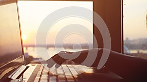 Close up of woman`s hands typing on laptop`s keyboard during beautiful sunset with sun lense flare effects.
