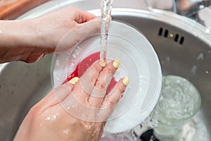 Close up woman`s hands of washing dishes in kitchen sink. Cleaning chores