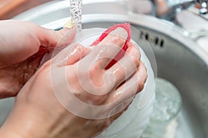 Close up woman`s hands of washing dishes in kitchen sink. Cleaning chores