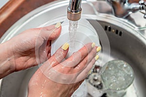 Close up woman`s hands of washing dishes in kitchen sink. Cleaning chores