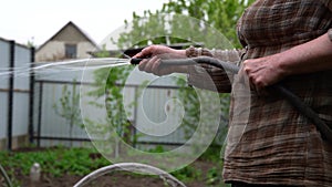 Close up of woman`s hands watering garden with hose. Older female courting of her household.