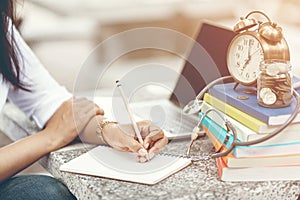 Close up of woman`s hands writing in spiral notepad placed on desktop.