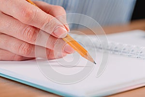 Close up of woman`s hands writing in spiral notepad placed on wooden desktop with various items