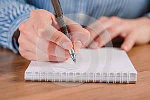 Close up of woman`s hands writing in spiral notepad placed on wooden desktop with various items