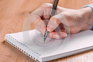 Close up of woman`s hands writing in spiral notepad placed on wooden desktop with various items